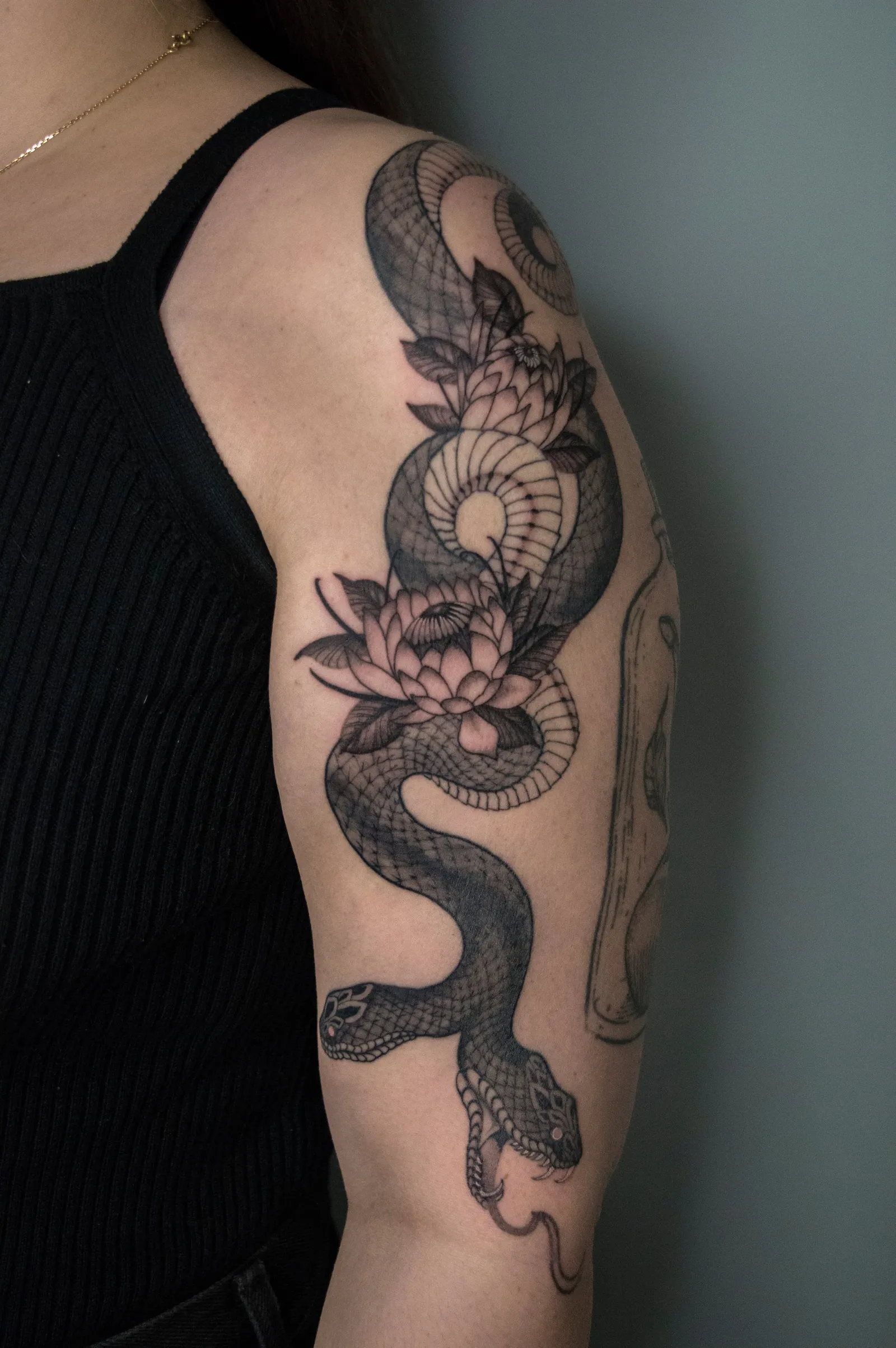 A snake coiled around lotus flowers down the outer arm, beside a corked glass bottle, black and grey
