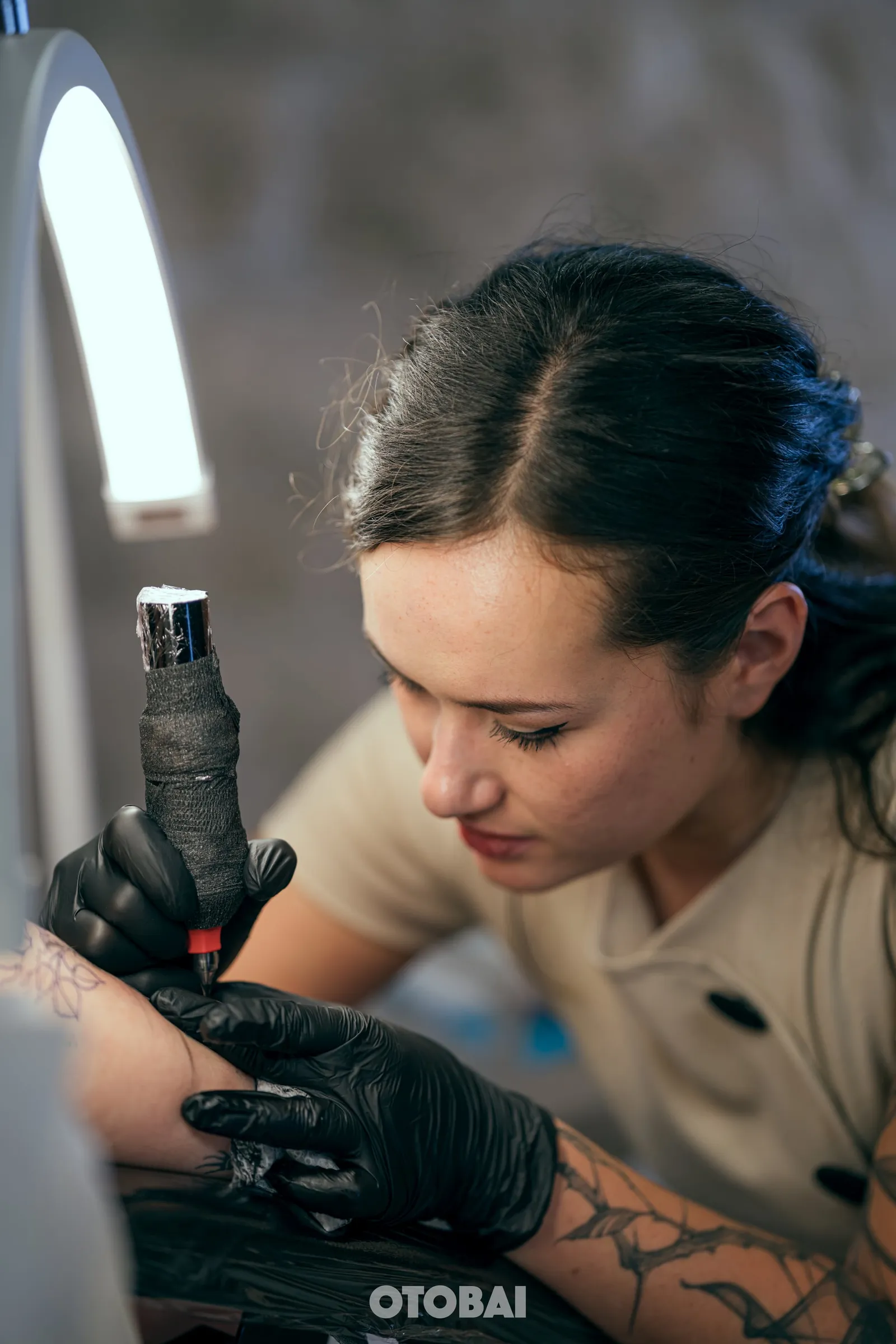 Joy tattooing, machine in her gloved hand, under the studio's ring light