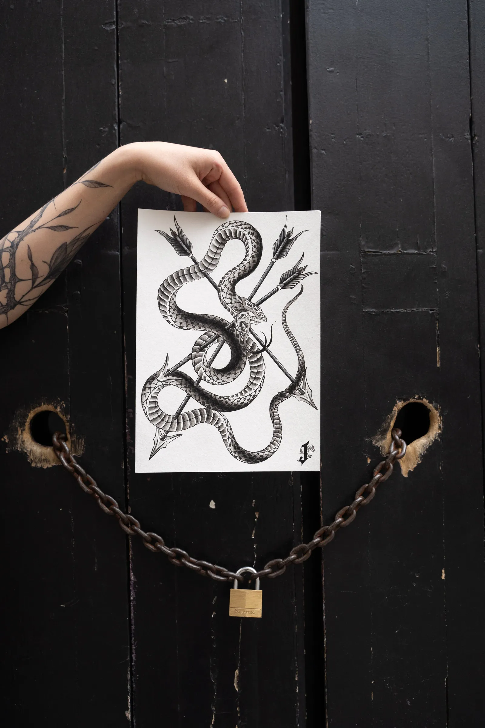 A hand holding the drawing against a black door with a padlocked chain: a snake knotted with three arrows