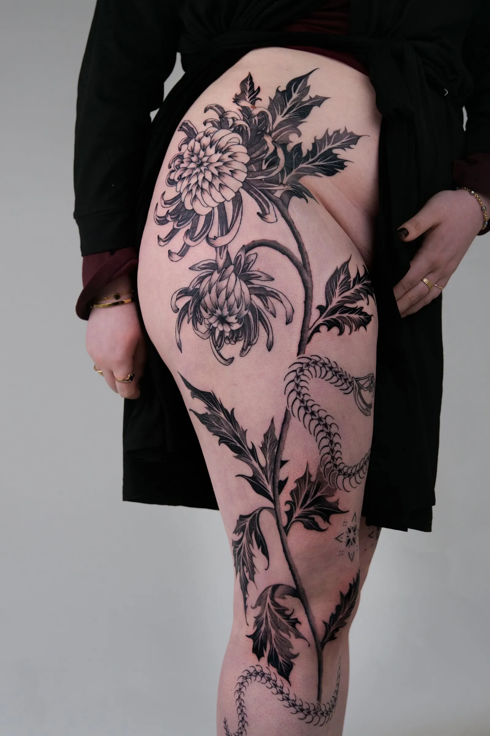 Chrysanthemums, thistle leaves and a snake skeleton running down the outer leg from hip to knee, black and grey