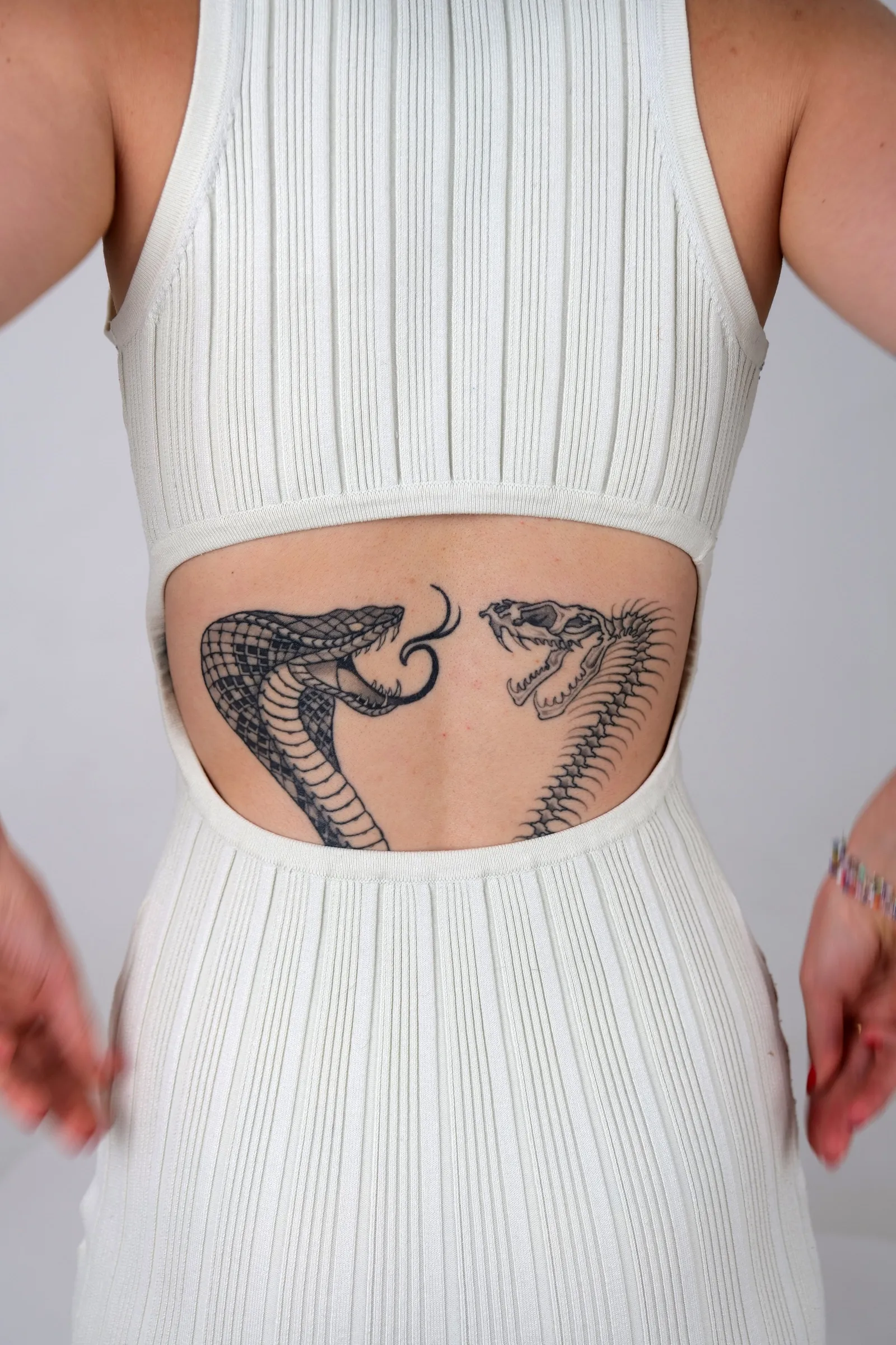 Two hooded cobras facing each other across a lower back, healed, framed by an open-backed dress