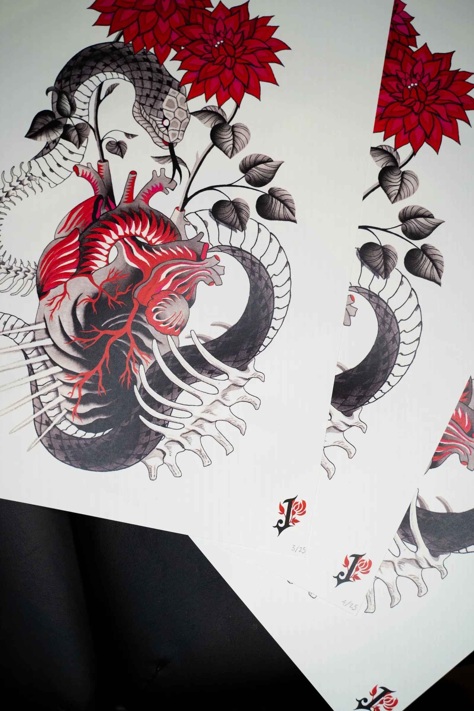 Prints of the painting fanned out: a red anatomical heart, a snake and ribs, red dahlias