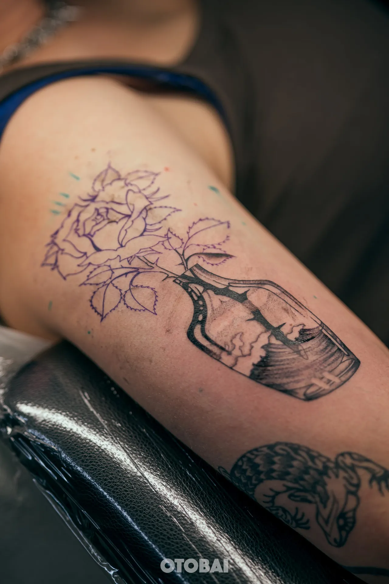 A violet stencil of flowers in a bottle on an arm, the bottle already lined in black