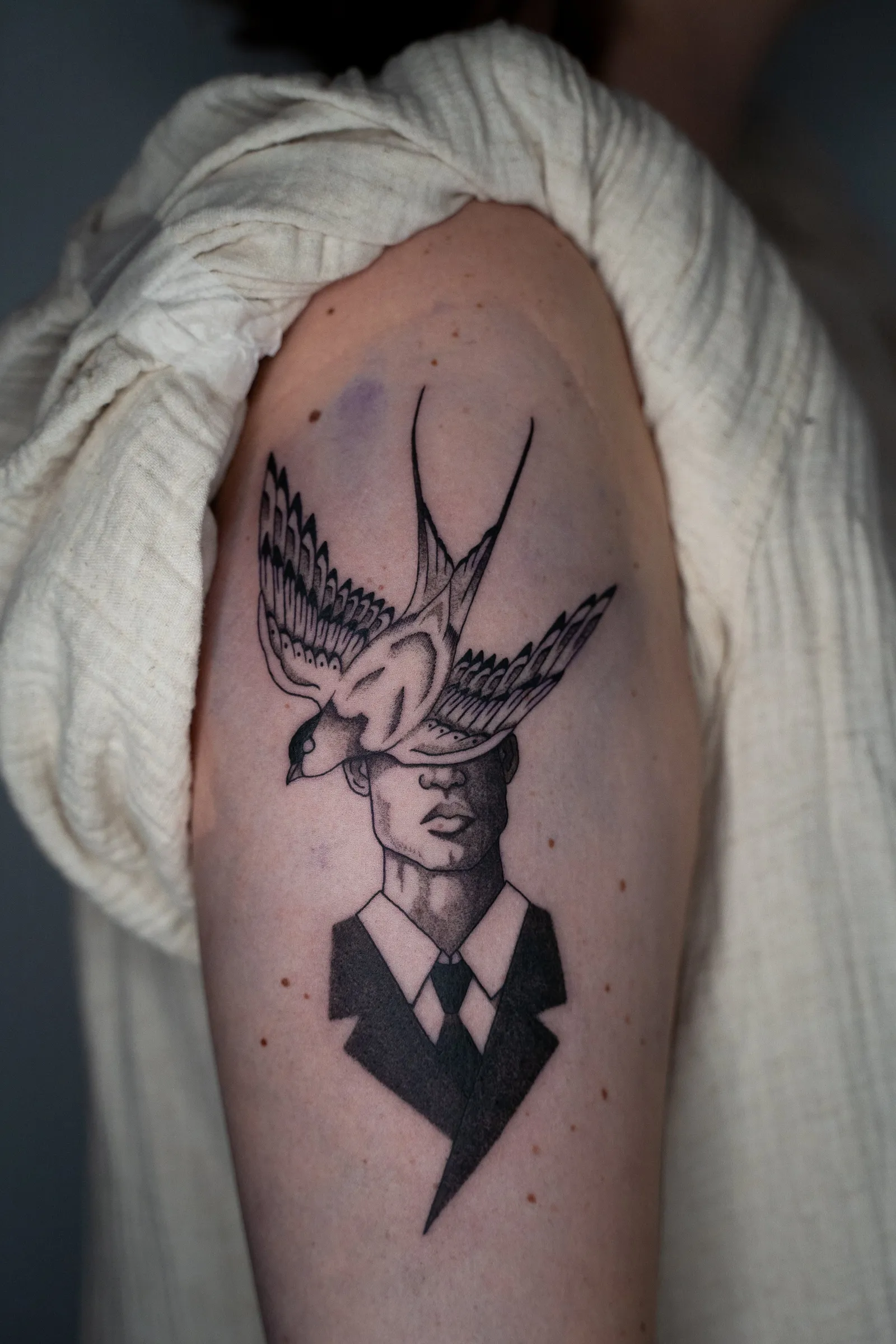 A man in a suit and tie whose head is a swallow in flight, tattooed on an upper arm