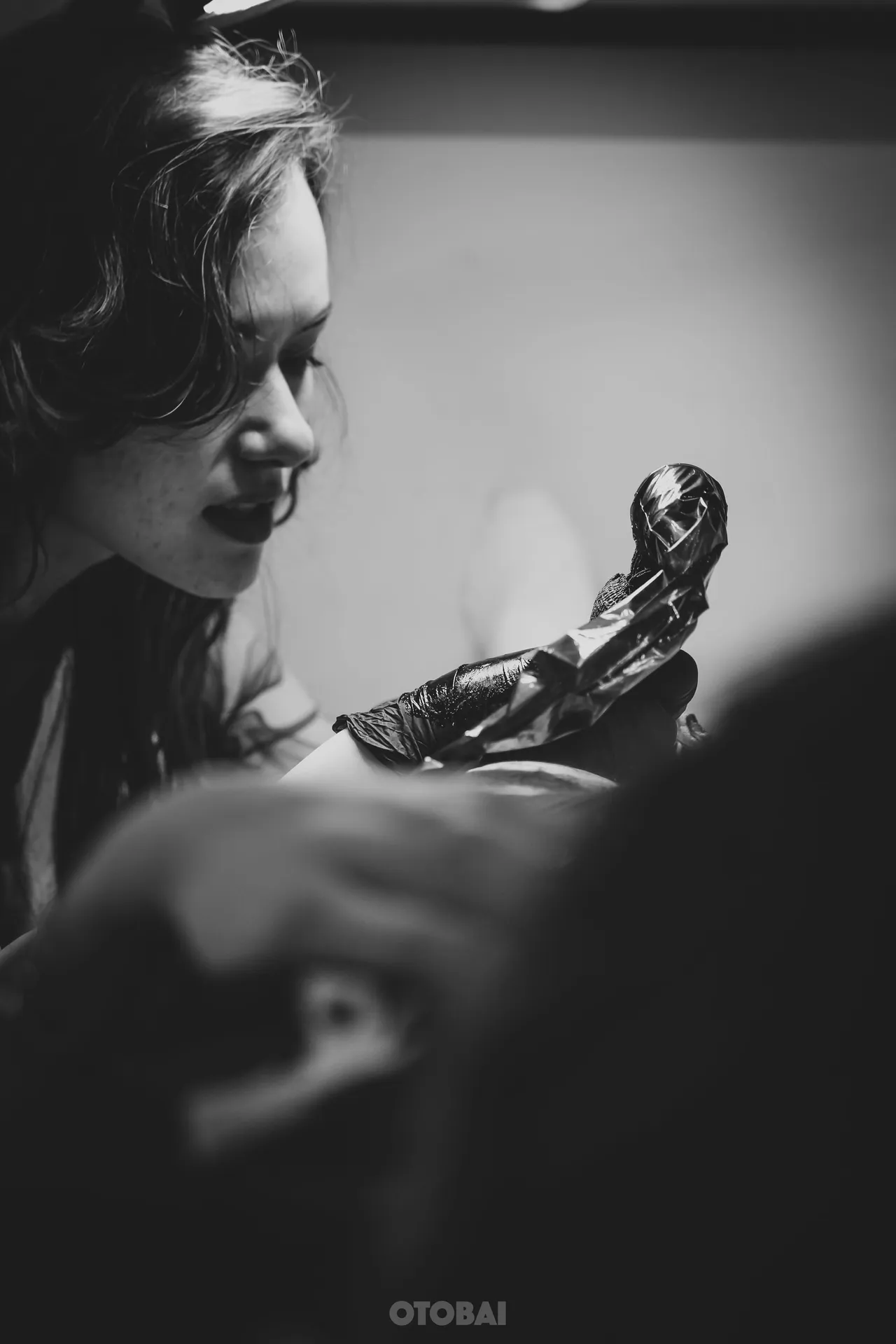 Joy smiling with her tattoo machine raised, in black and white