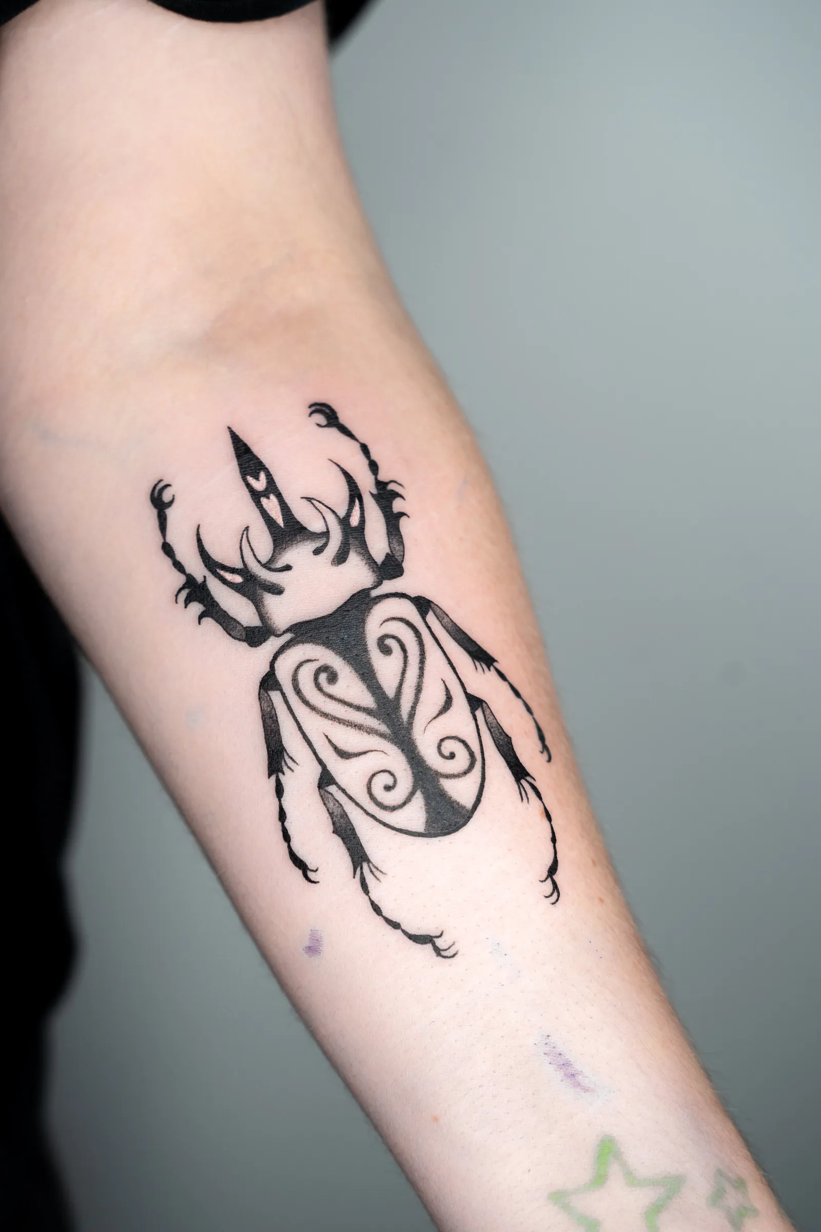 A scarab beetle with ornamented wing cases, tattooed in bold black and fine line on a forearm