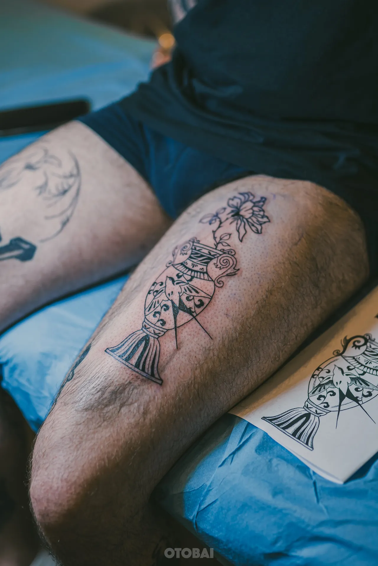 A thigh with the flower vase stencil and its first black lines, the paper stencil beside it