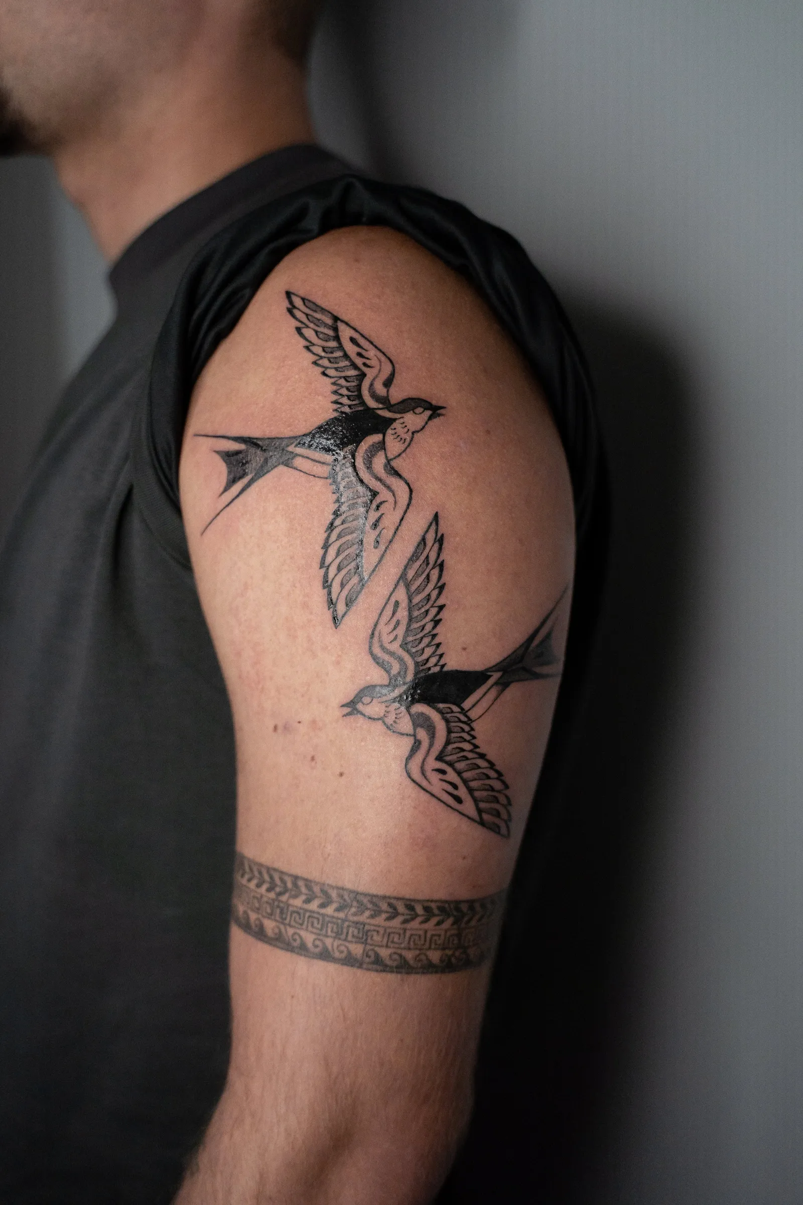 Two swallows in flight, one above the other, tattooed on an upper arm