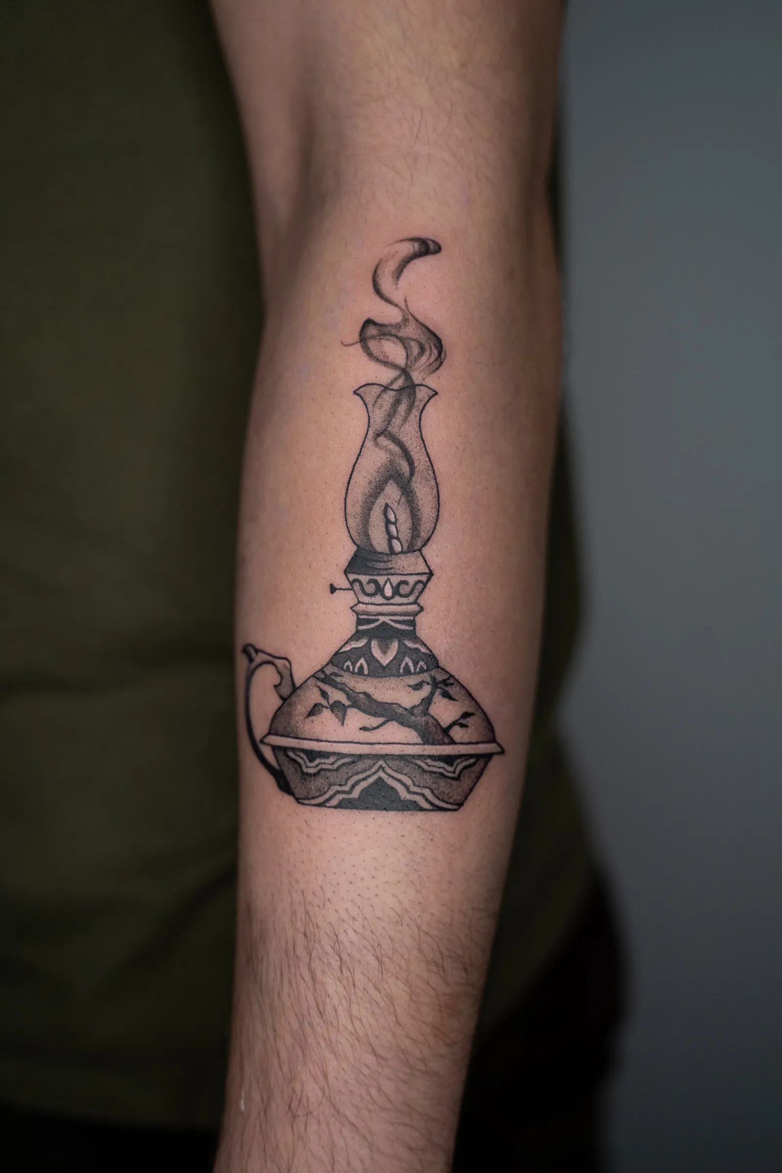 An ornate oil lamp with a tall flame, tattooed on a forearm