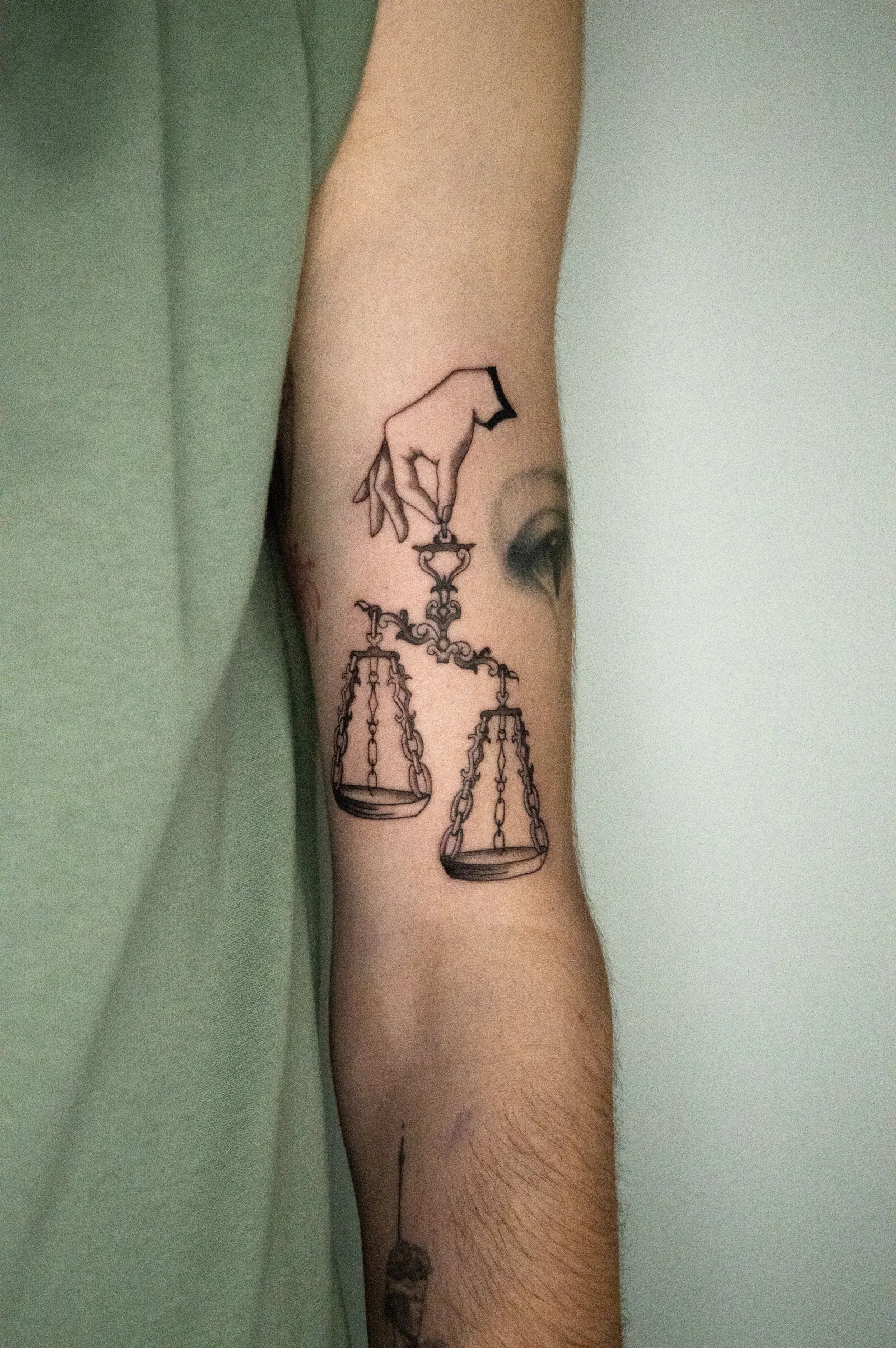 A hand holding a pair of balance scales by a thread, fine line on an inner arm