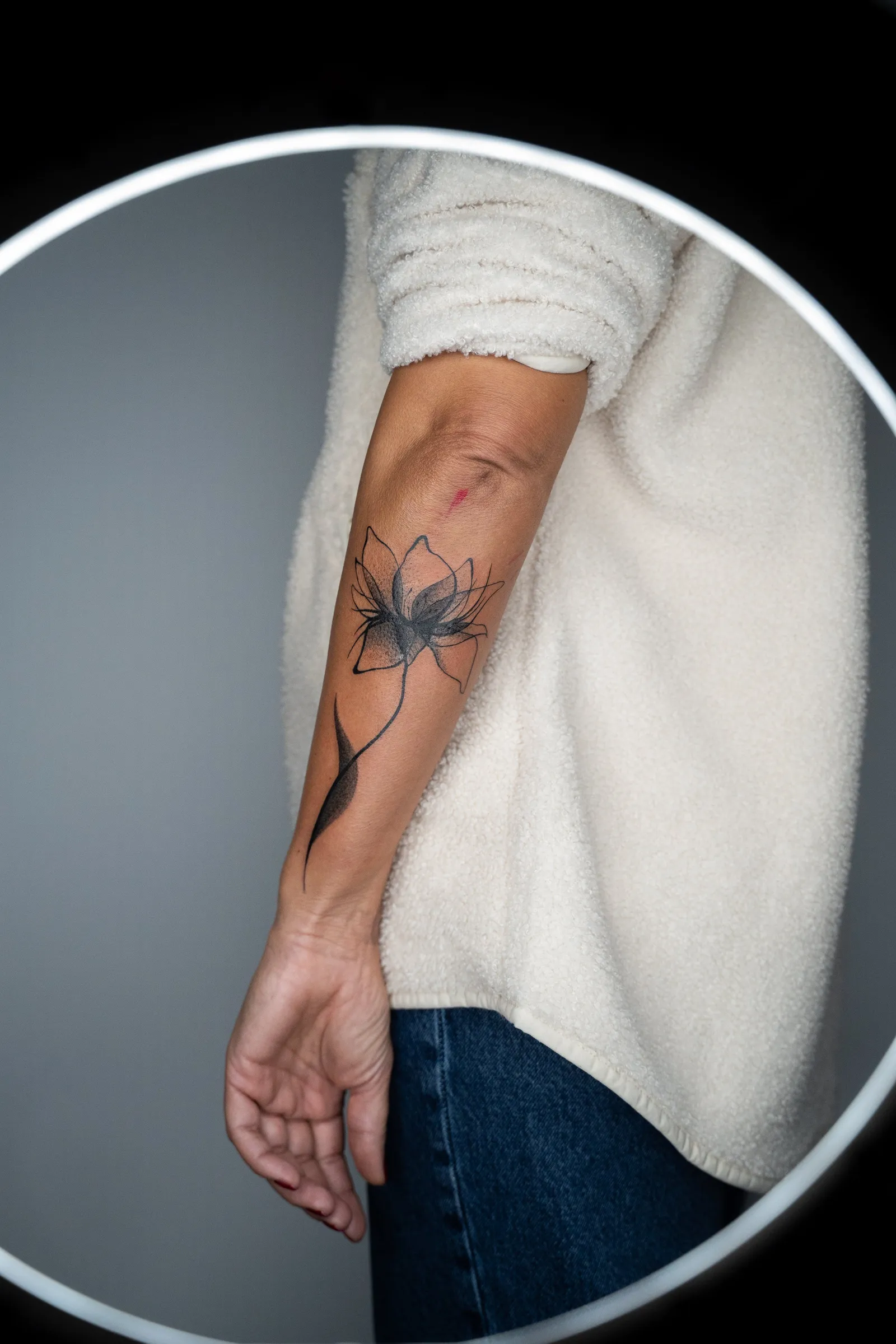 A single lotus flower on a long stem, tattooed in fine line and soft shading along a forearm