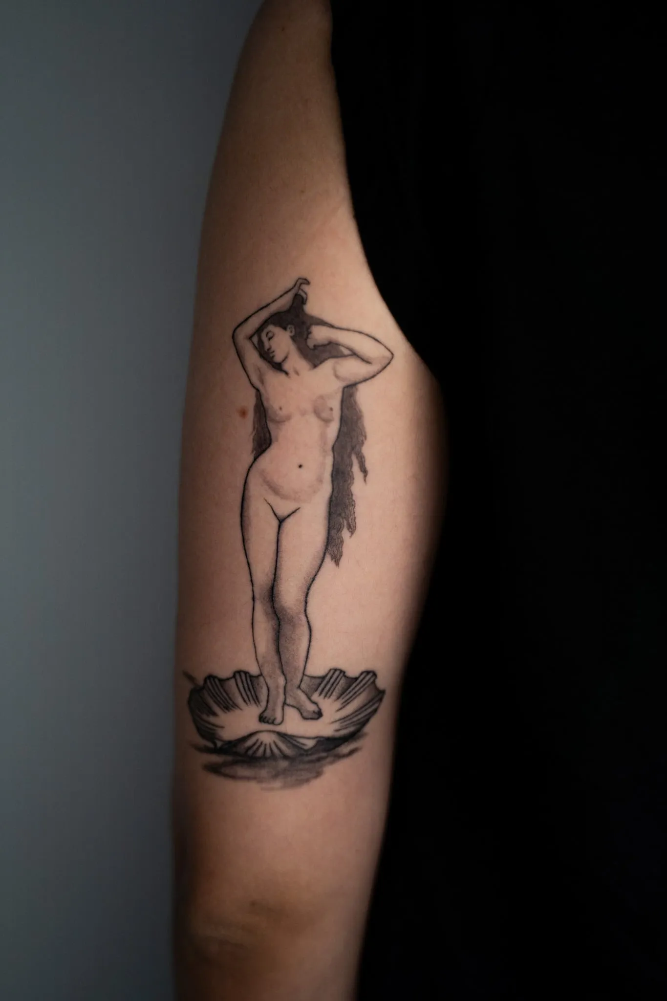 Venus standing on a scallop shell, after Botticelli, tattooed in black and grey on a forearm